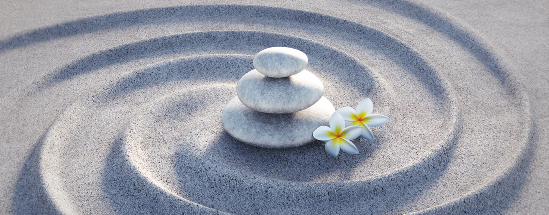 Three stones stacked and two flower petals on smooth sand.